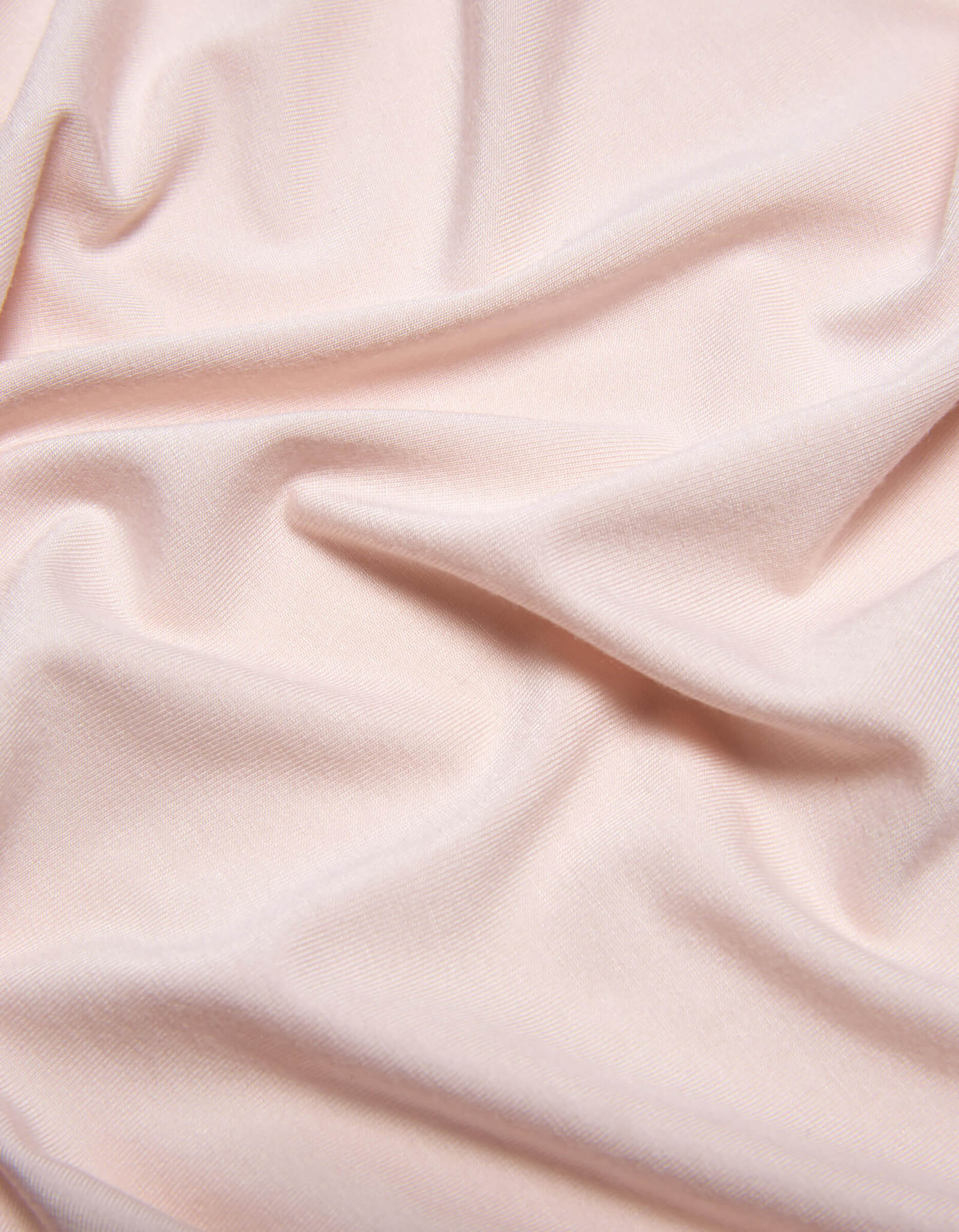 The Bamboo Jersey Sheet Set by Cozy Earth features soft, light pink fabric with subtle folds and gentle wrinkles for a smooth, slightly textured look.