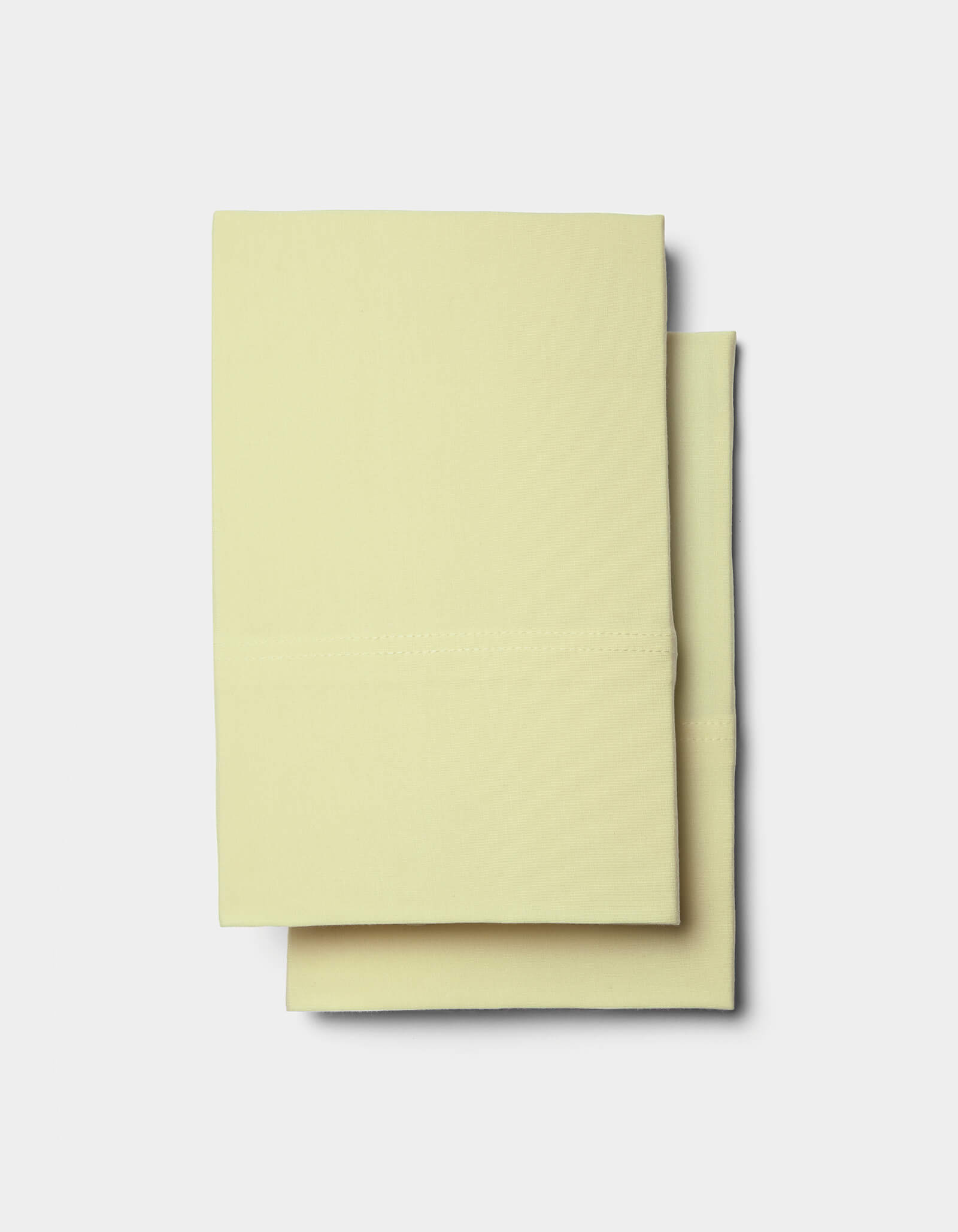 Two neatly folded Bamboo Jersey Sheet Sets by Cozy Earth in pale yellow are stacked on a plain white background.