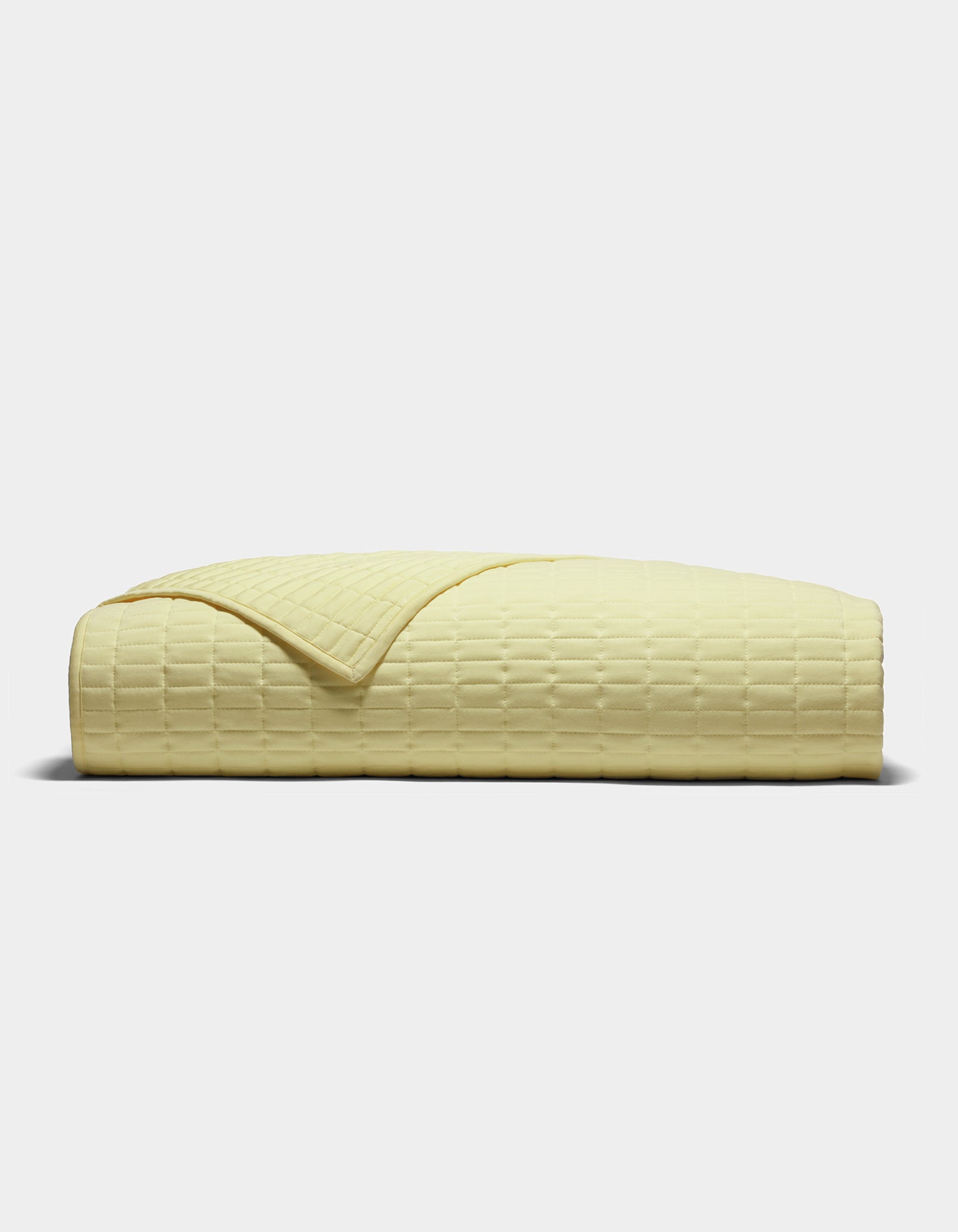 The Cozy Earth Bamboo Jersey Quilt, shown folded from the side on a plain light background, features a pale yellow color and a subtle grid-like textured pattern.|Color:Meringue