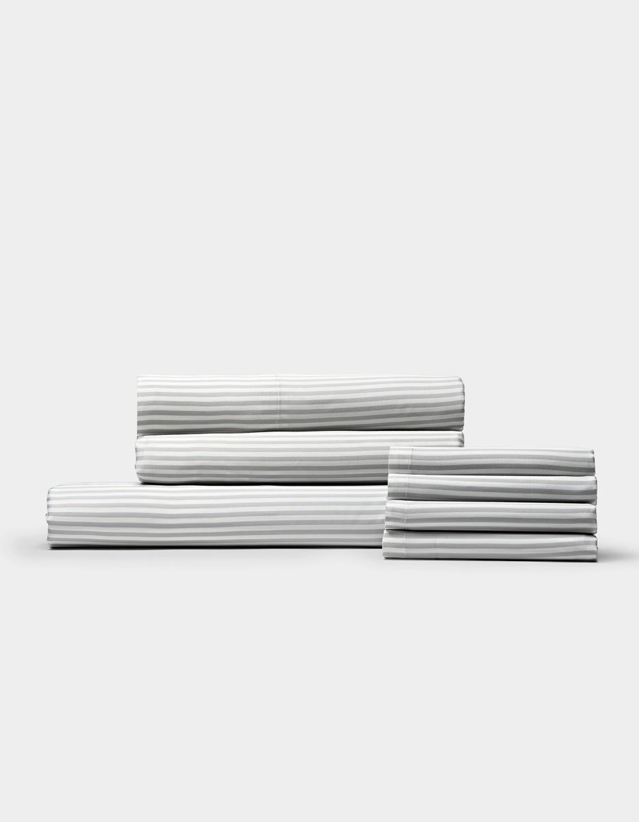A neatly stacked set of Cozy Earth Bamboo Bedding Core Bundle sheets, featuring white fabric with thin grey stripes, displayed against a plain light background.