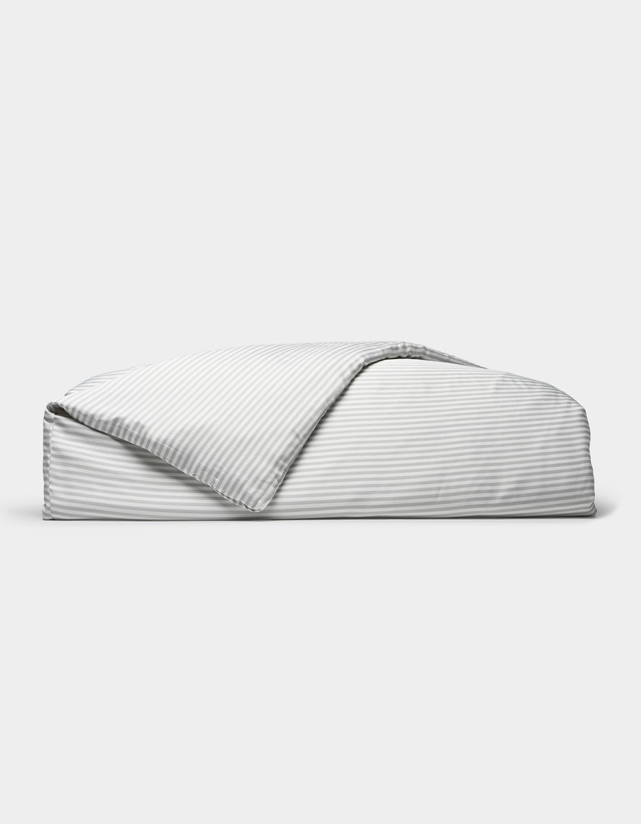 A neatly folded Bamboo Duvet Cover by Cozy Earth, featuring light gray and white stripes with one corner flipped open, is displayed against a plain white background.|Color:Classic Stripe in Dew