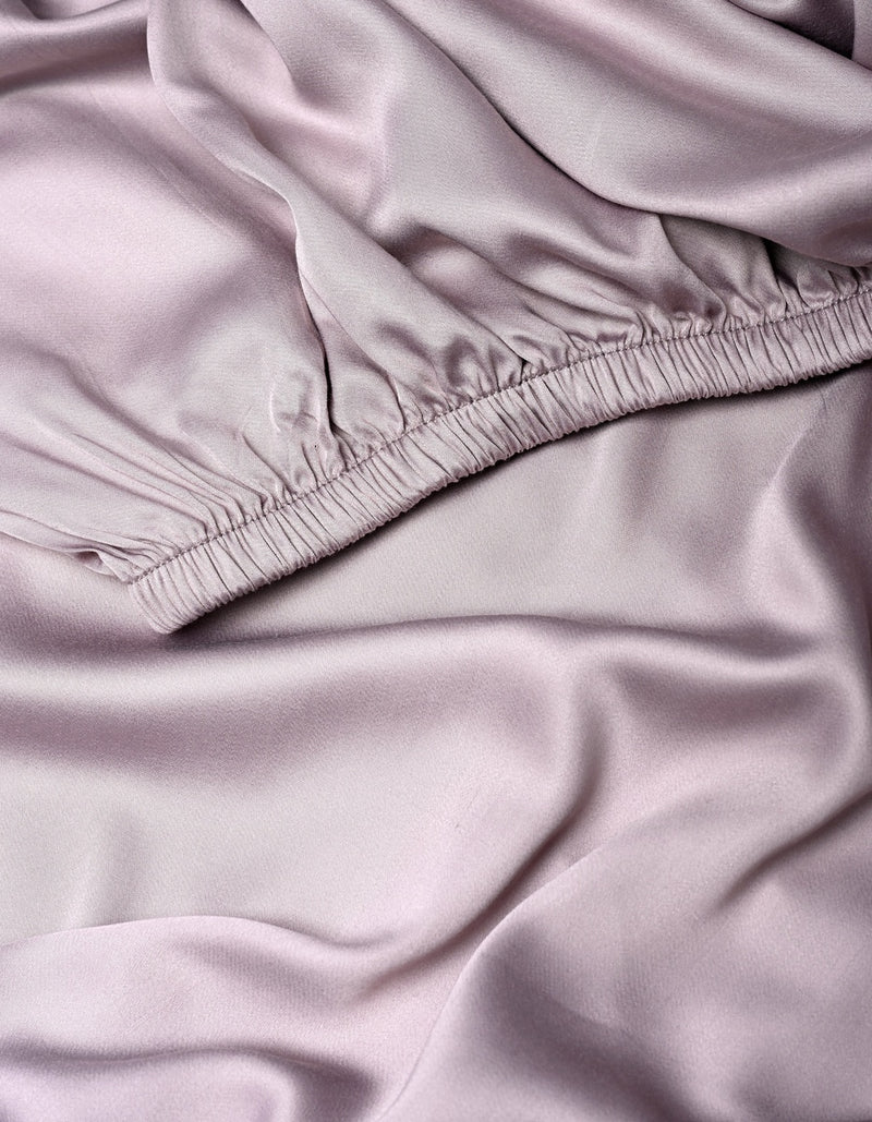 Close-up of soft, light lavender Bamboo Fitted Sheet by Cozy Earth, featuring a gathered, ruched elastic seam at the top and smooth, flowing folds below.