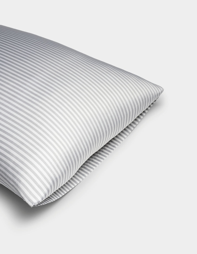 A close-up of a Bamboo Pillowcase by Cozy Earth, featuring gray and white vertical stripes, set against a plain white background.