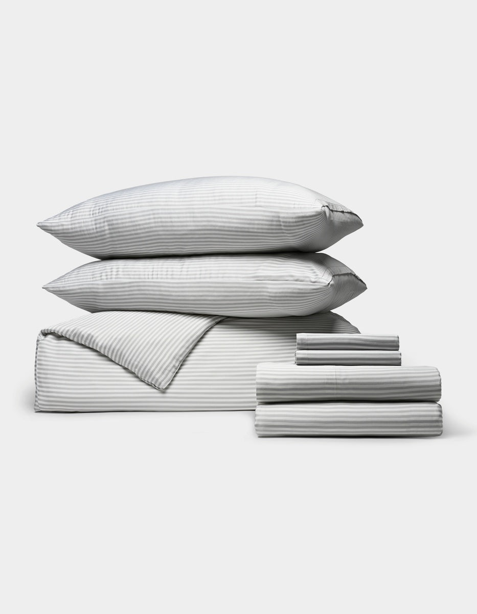 A neatly stacked set of Cozy Earth’s Bamboo Bedding Ultimate Bundle, featuring two pillows, a folded comforter, and two stacks of folded sheets in gray and white stripes, displayed on a light gray background.
