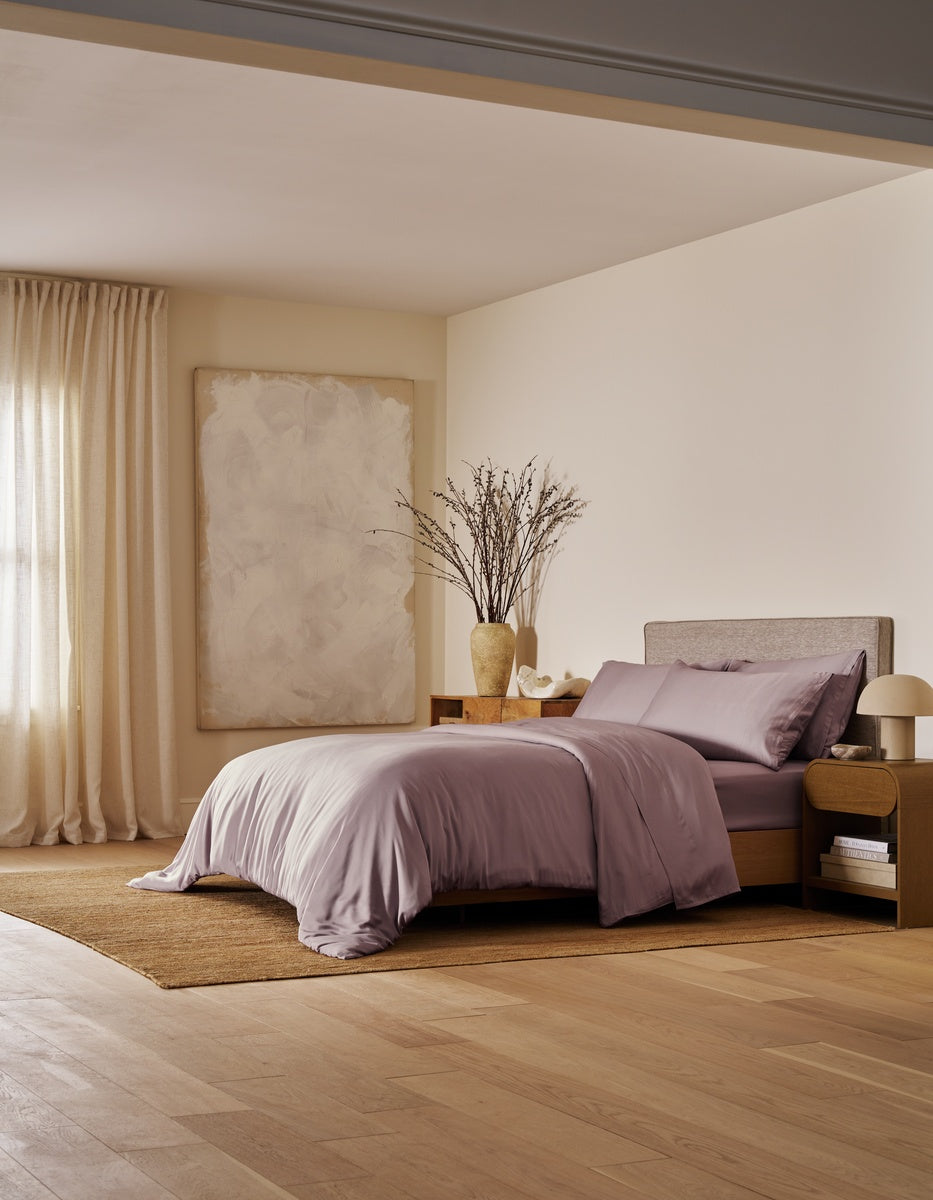 A modern bedroom featuring the Cozy Earth Bamboo Bedding Ultimate Bundle, complemented by neutral walls, large abstract artwork, a floor vase with branches, beige curtains, a wooden nightstand, and bathed in soft natural light.
