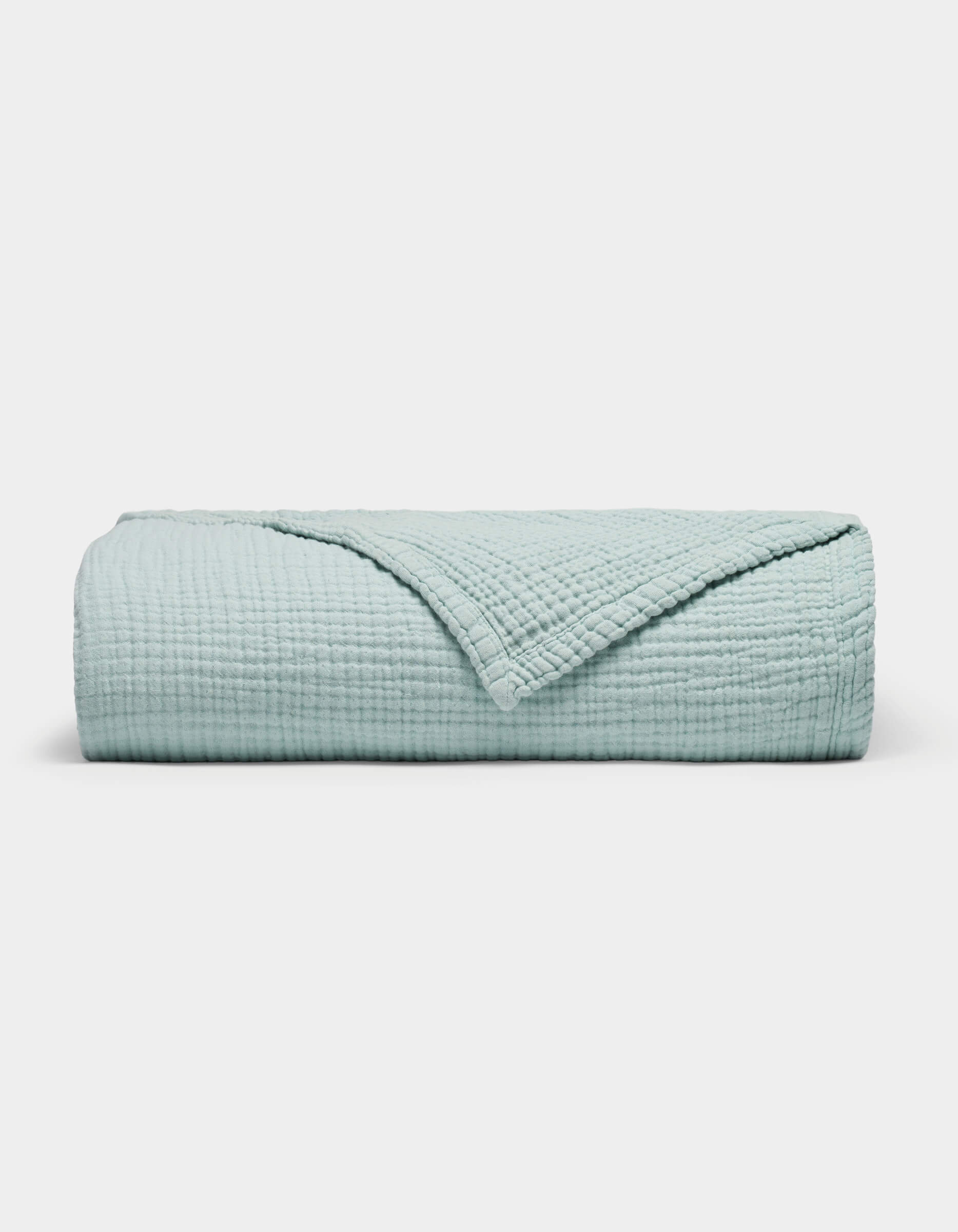 The Cozy Earth Cotton Gauze Blanket is neatly folded in light blue with a textured, grid-like pattern on a plain white background. One corner is turned down to reveal the inner side.