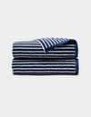 A Ribbed Terry Bath Towel by Cozy Earth, navy blue with white horizontal stripes, is neatly folded and displayed on a light gray background.|Color:Obsidian Stripe