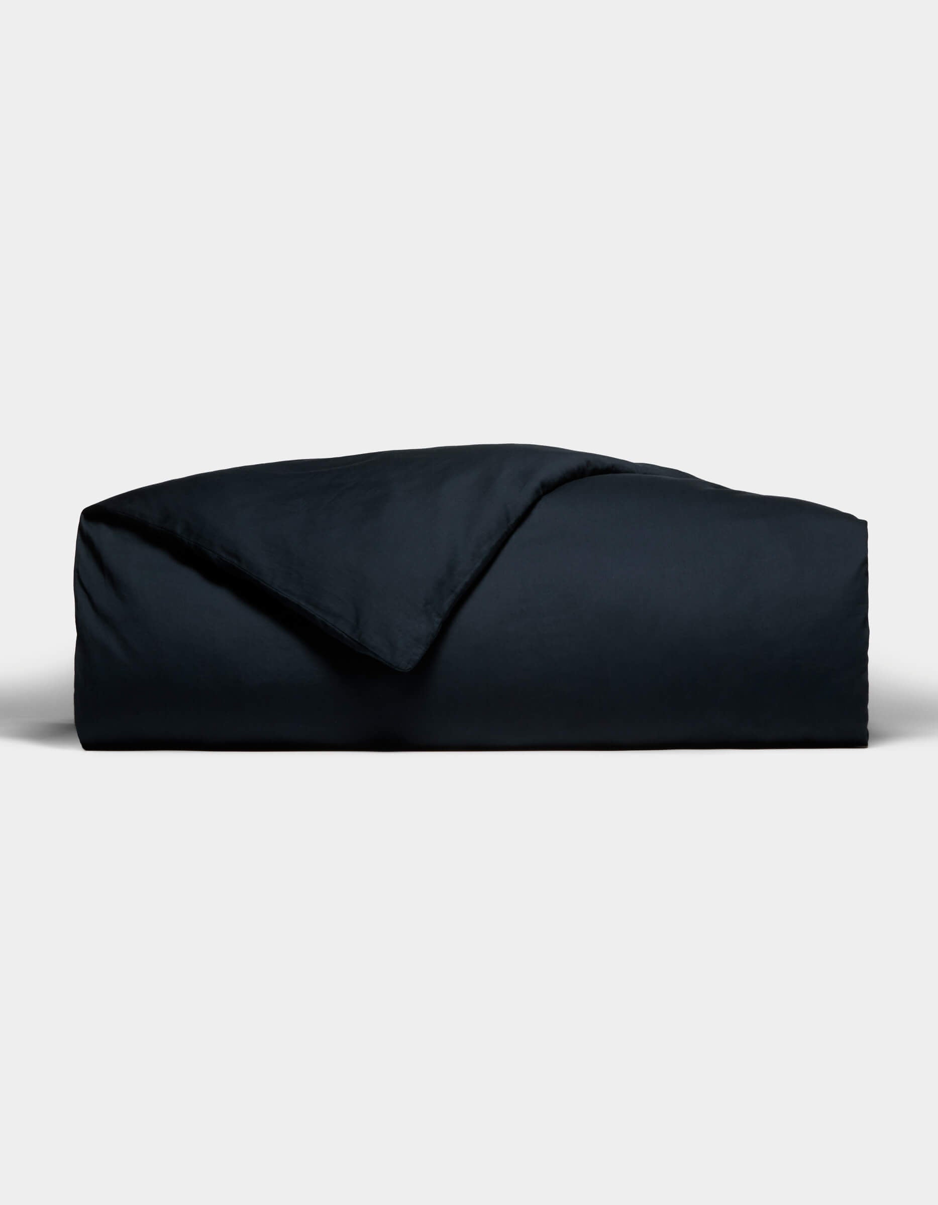 The Cozy Earth Soft-Wash Cotton Duvet Cover, in a dark hue, is neatly folded with one corner flipped to reveal its smooth texture, set against a plain light gray background.|Color:Eclipse