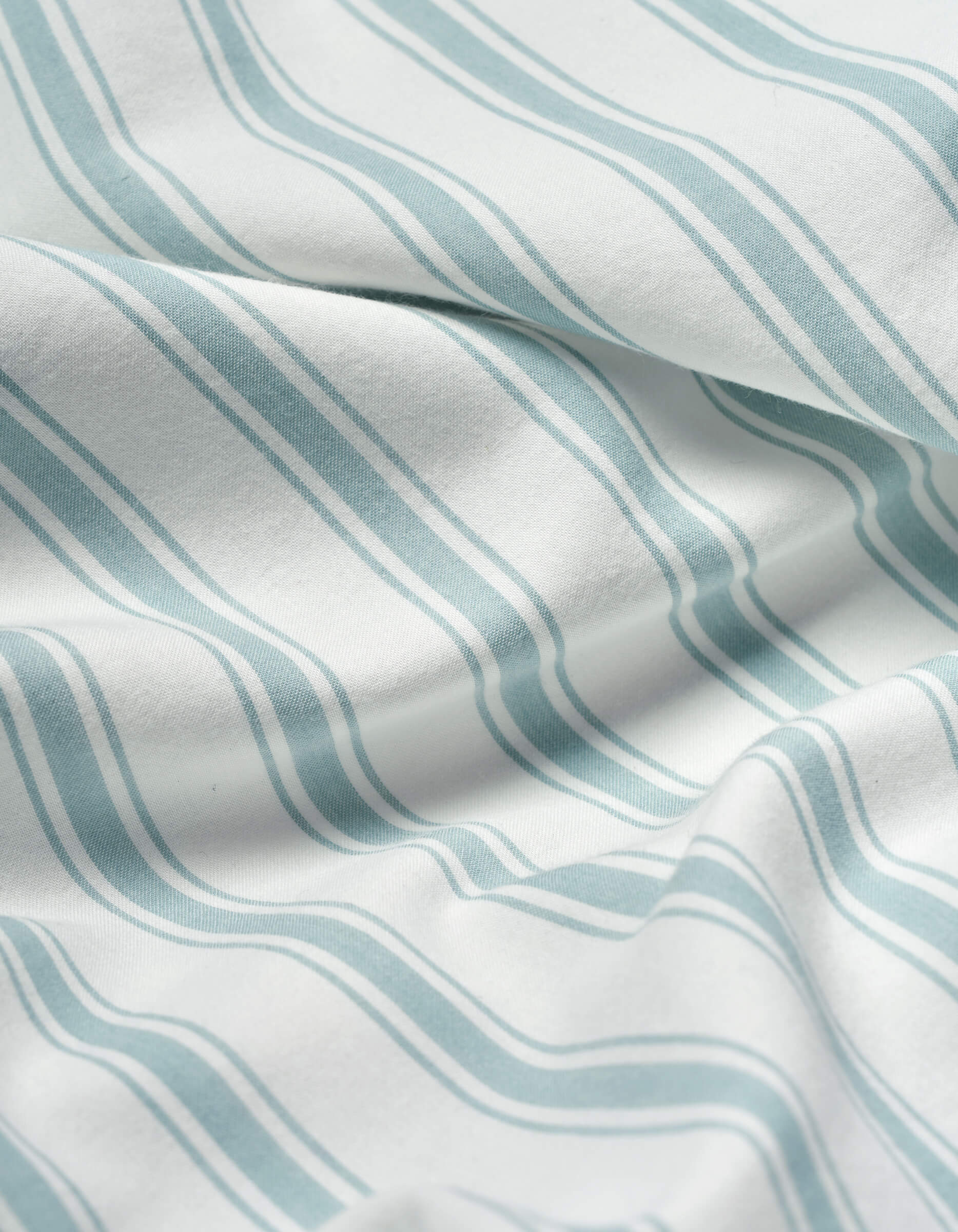Close-up of Cozy Earth Soft-Wash Cotton Flat Sheet: white fabric with soft, wavy blue-green stripes and slight wrinkles that create gentle shadows and texture.