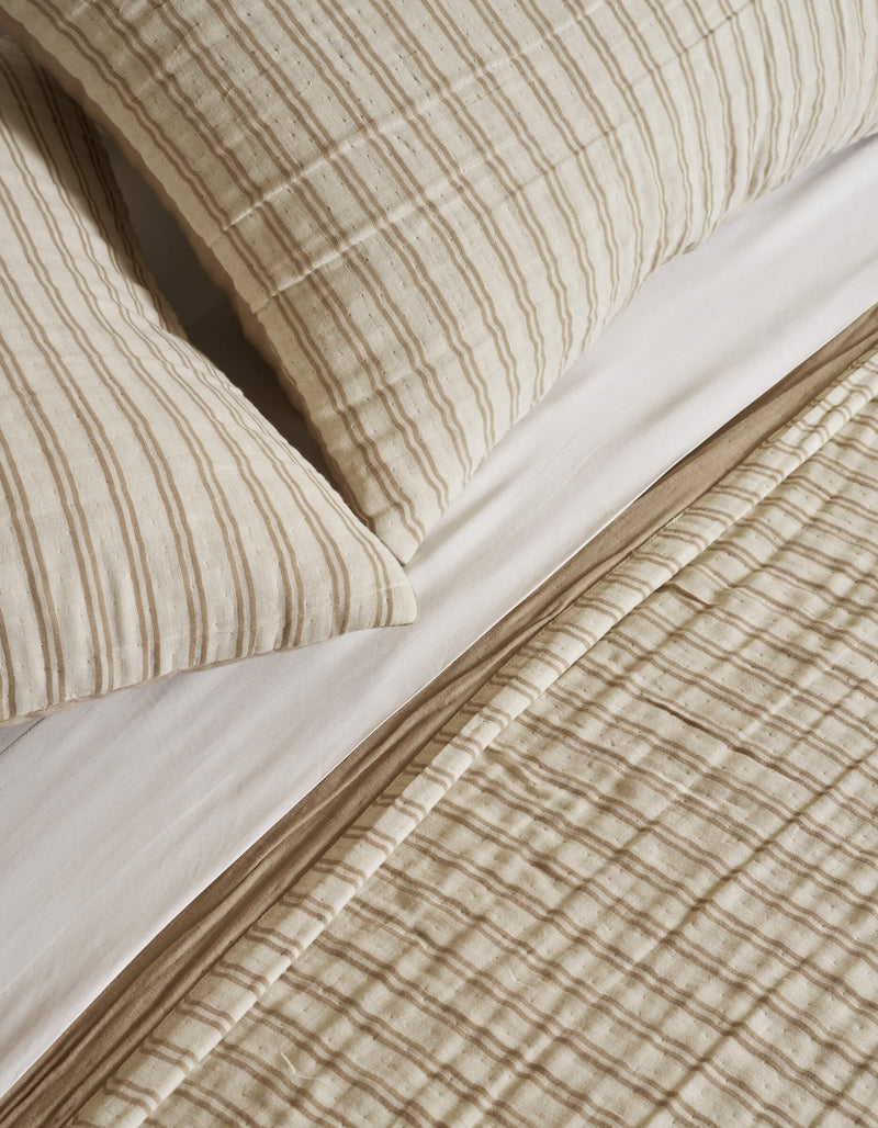 Close-up of Cozy Earth's Waterfront Coverlet Bundle—a neatly made bed with striped pillows, a quilted blanket, and a white sheet, all in soft, textured fabric.