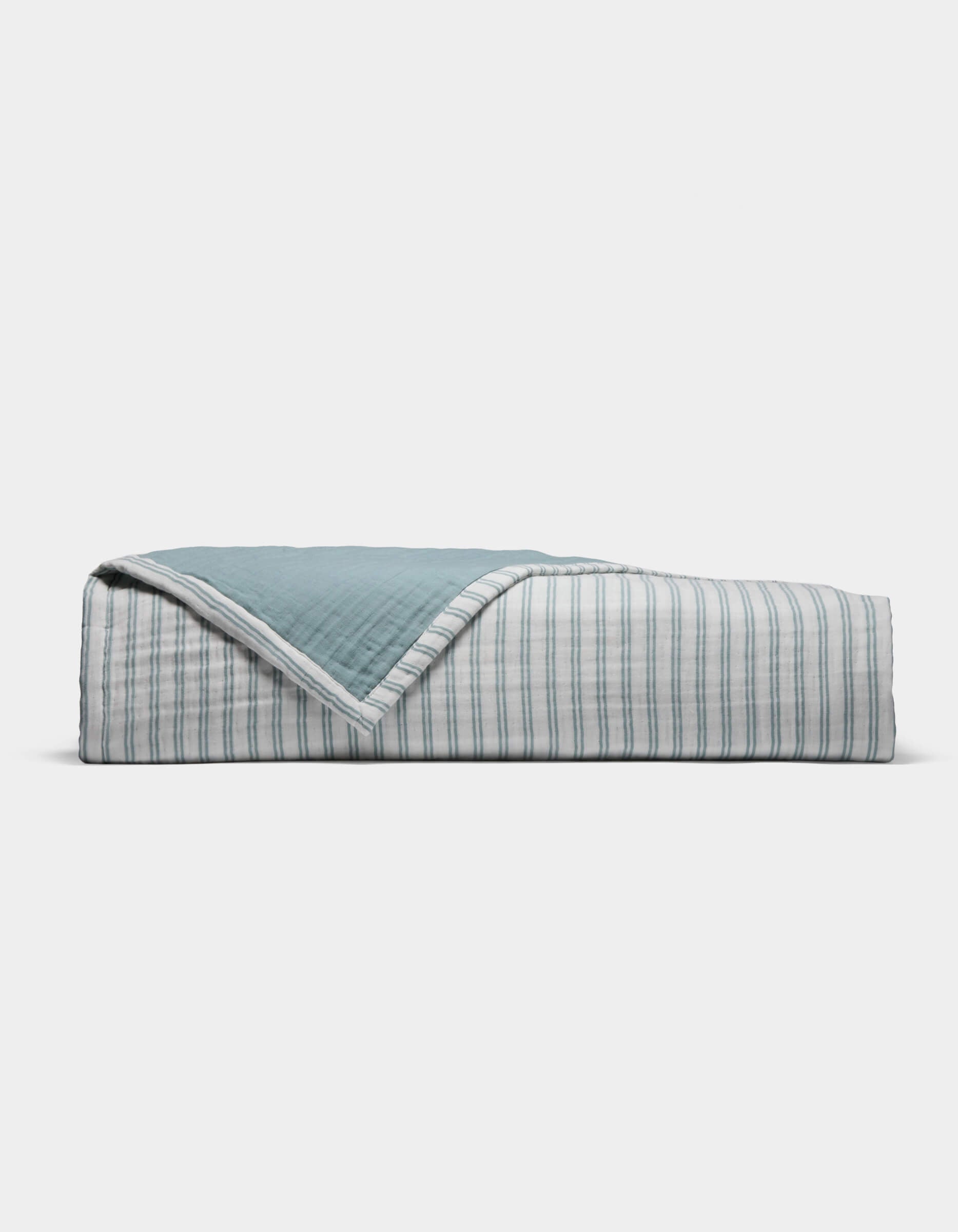 The Cozy Earth Waterfront Coverlet is a neatly folded quilt with a blue top and a white underside featuring thin blue stripes, displayed against a plain white background.