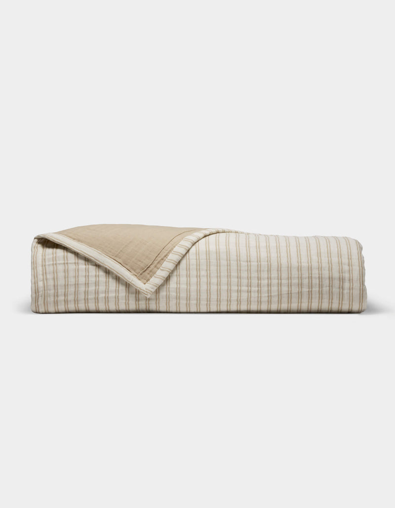 The Cozy Earth Waterfront Coverlet, featuring beige and white stripes on one side and solid beige on the reverse, is shown neatly folded against a simple light backdrop.