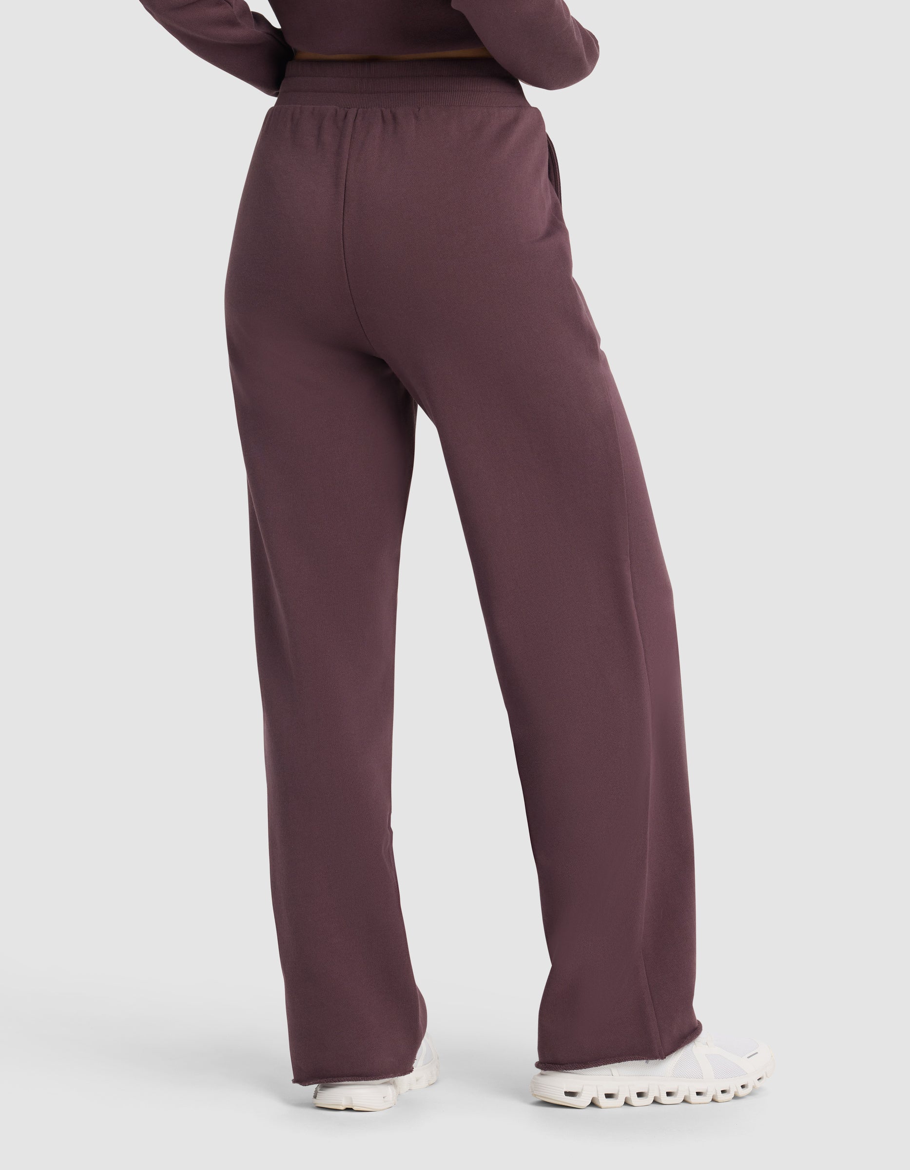 A person is shown from the back wearing Cozy Earth's Chelsea Pant in maroon, a loose-fitting, high-waisted style, paired with white sneakers and arms at their sides.