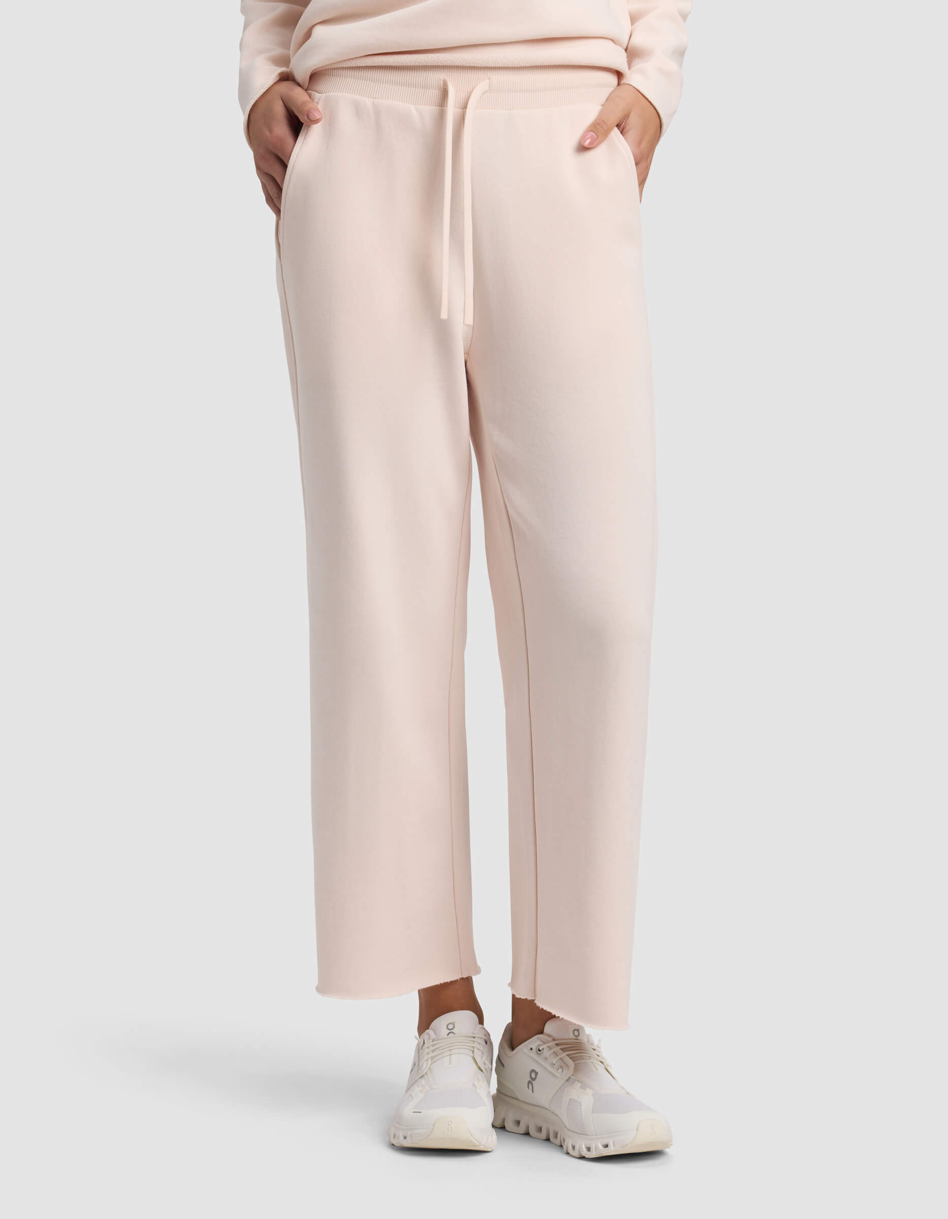 A person wears Cozy Earth Women's Chelsea Cropped Pant in light pink, styled with white sneakers and hands in pockets, against a plain light background.|Color:Petal