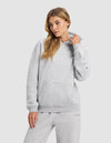 A woman wears the Cozy Earth Women's Cityscape 2.0 Hoodie in light gray, standing against a plain background and looking to the side as she adjusts her collar.|Color:Heather Grey