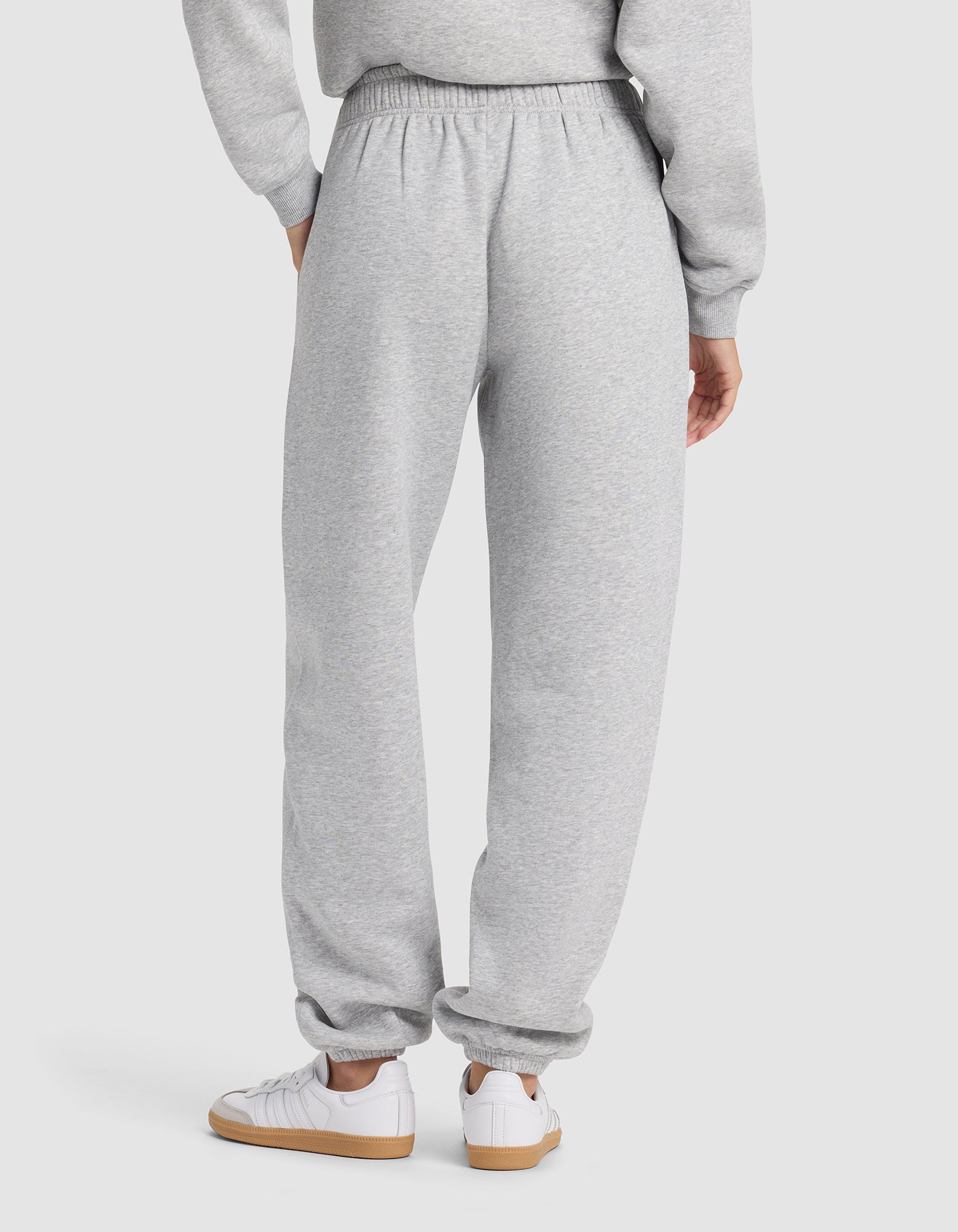 A person is shown from the back wearing Cozy Earth's Women's Cityscape 2.0 Sweatpant in light gray with a matching sweatshirt and white sneakers with tan soles, against a plain, light-colored background.