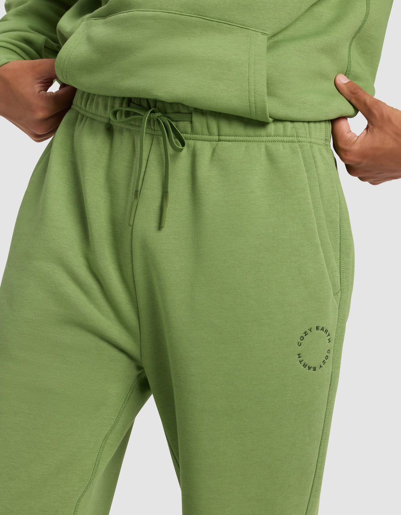A person wears Cozy Earth Men's Cityscape Sweatpant in light green with an elastic drawstring waistband, a small circular logo by the left pocket, and a matching sweatshirt, one hand in the pocket.