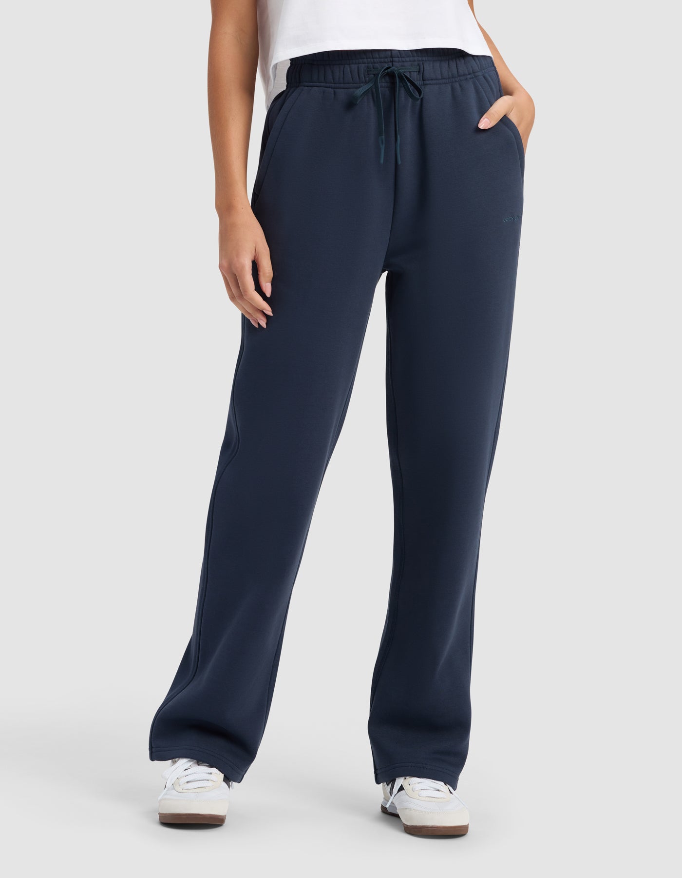 A person wearing Cozy Earth Women's Cityscape 2.0 Wide Leg Pant in navy, a white shirt, and white sneakers stands with hands in their pockets against a plain light gray background.