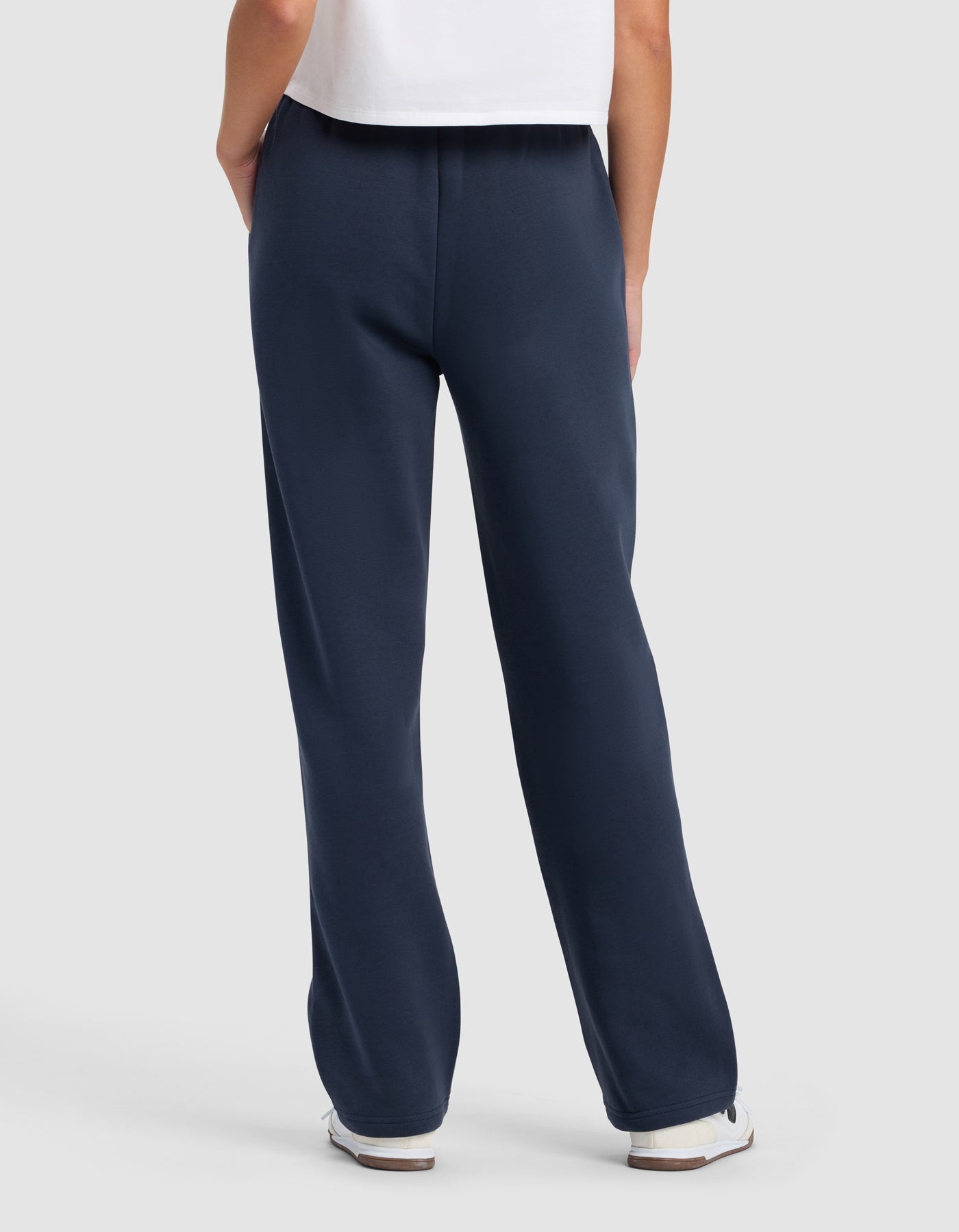 A person faces away, wearing Cozy Earth's Women's Cityscape 2.0 Wide Leg Pant in navy, paired with a white t-shirt and white sneakers, set against a plain light background.