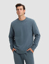 A man wears the Cozy Earth Men's Dylan Crewneck in blue-gray, standing with hands in pockets and facing the camera against a plain light gray background.|Color:Dawn