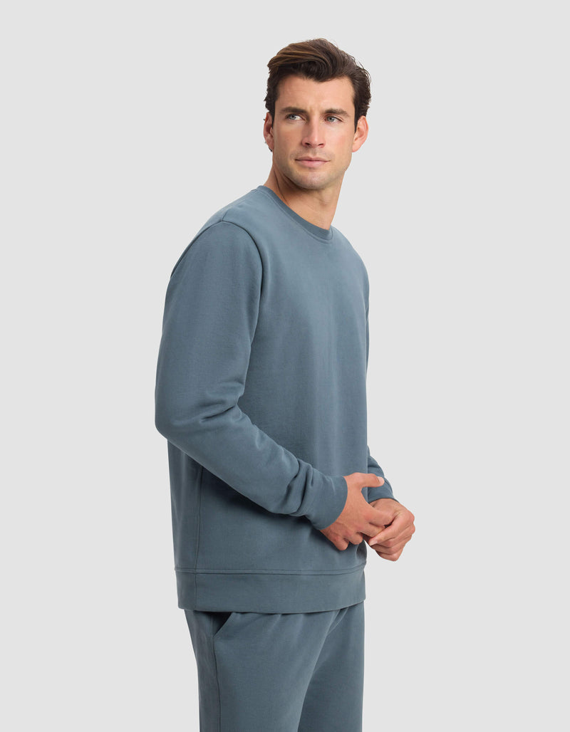 A man wearing the Cozy Earth Men's Dylan Crewneck stands against a plain light gray background, looking slightly to his left with a neutral expression.