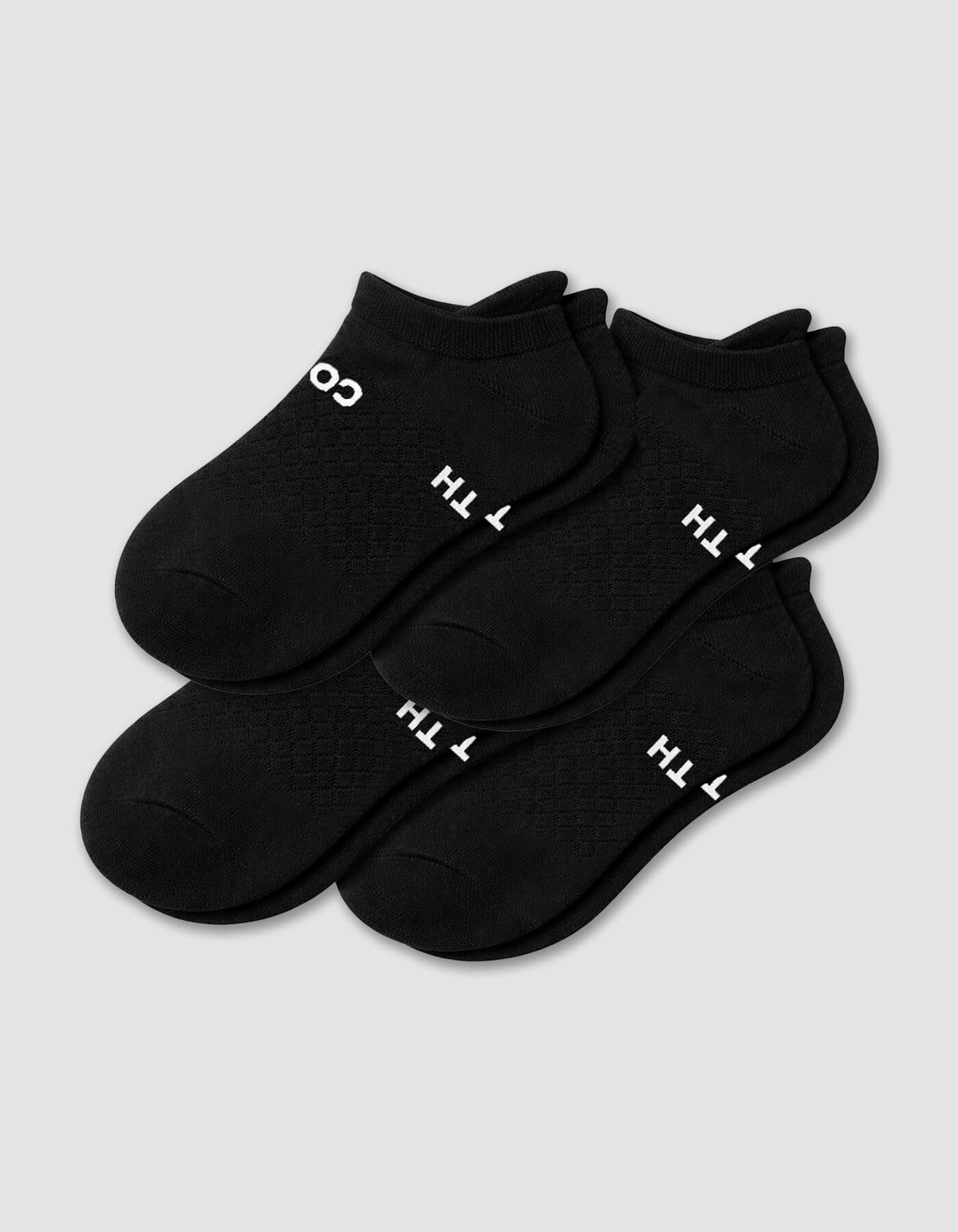 The Cozy Earth Men's Essential Ankle Sock 4-Pack in black features textured socks with partial white text on the soles, neatly stacked on a light gray background.|Color:Black