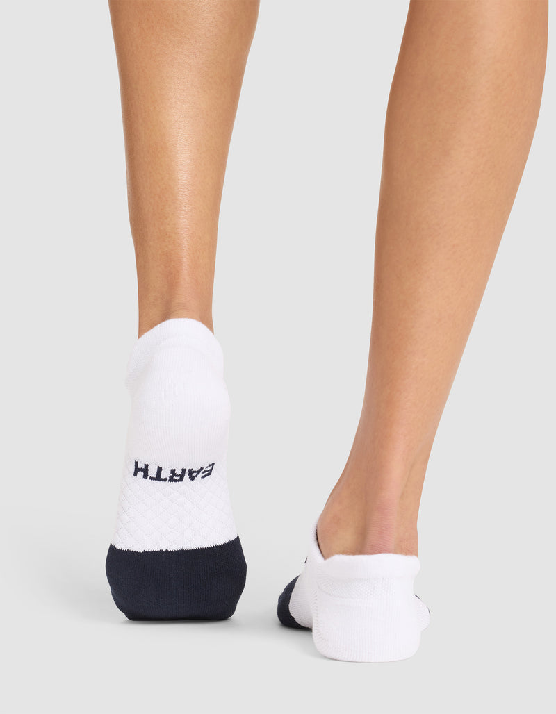 Back view of a person wearing Cozy Earth's Essential Ankle Socks in white and navy, with "EARTH" on the heel, standing on a light gray surface.