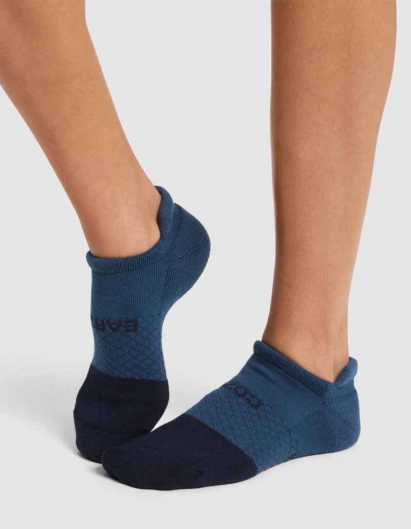 A person wears Cozy Earth's Essential Ankle Socks in blue and navy, standing with feet crossed against a light background.