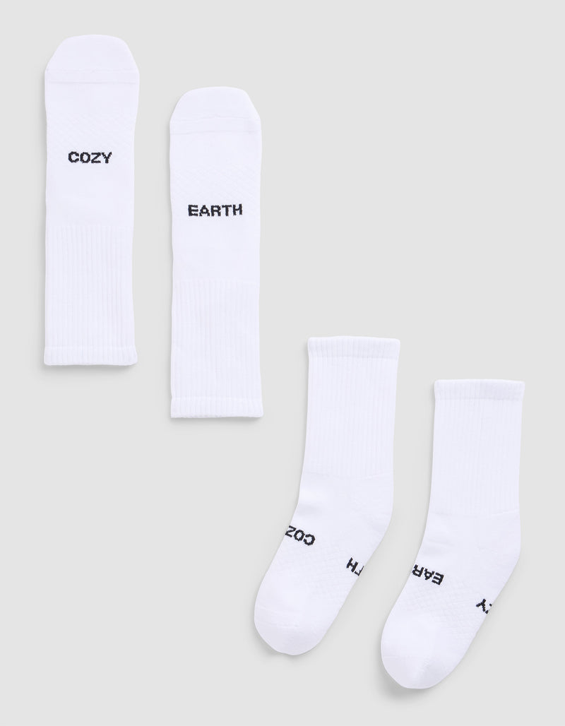 Four Essential Calf Socks by Cozy Earth are displayed on a light gray surface. Each white ribbed sock features black text: two say "COZY," and two say "EARTH." The socks are arranged flat and side by side.