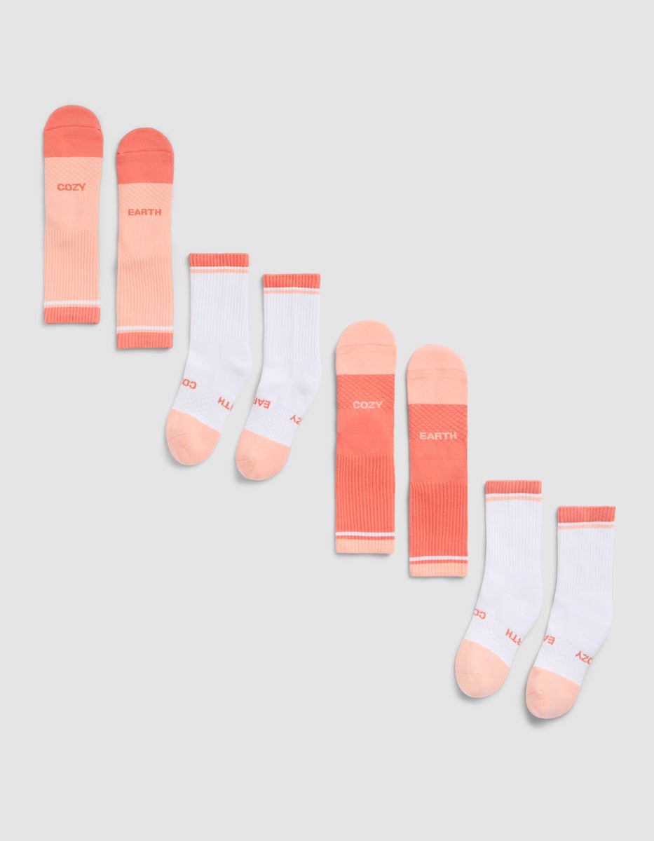The Cozy Earth Essential Calf Sock 4-Pack, in pink and white shades with "COZY" and "EARTH" near the toes, is arranged diagonally on a light gray background. |Color:Cantaloupe
