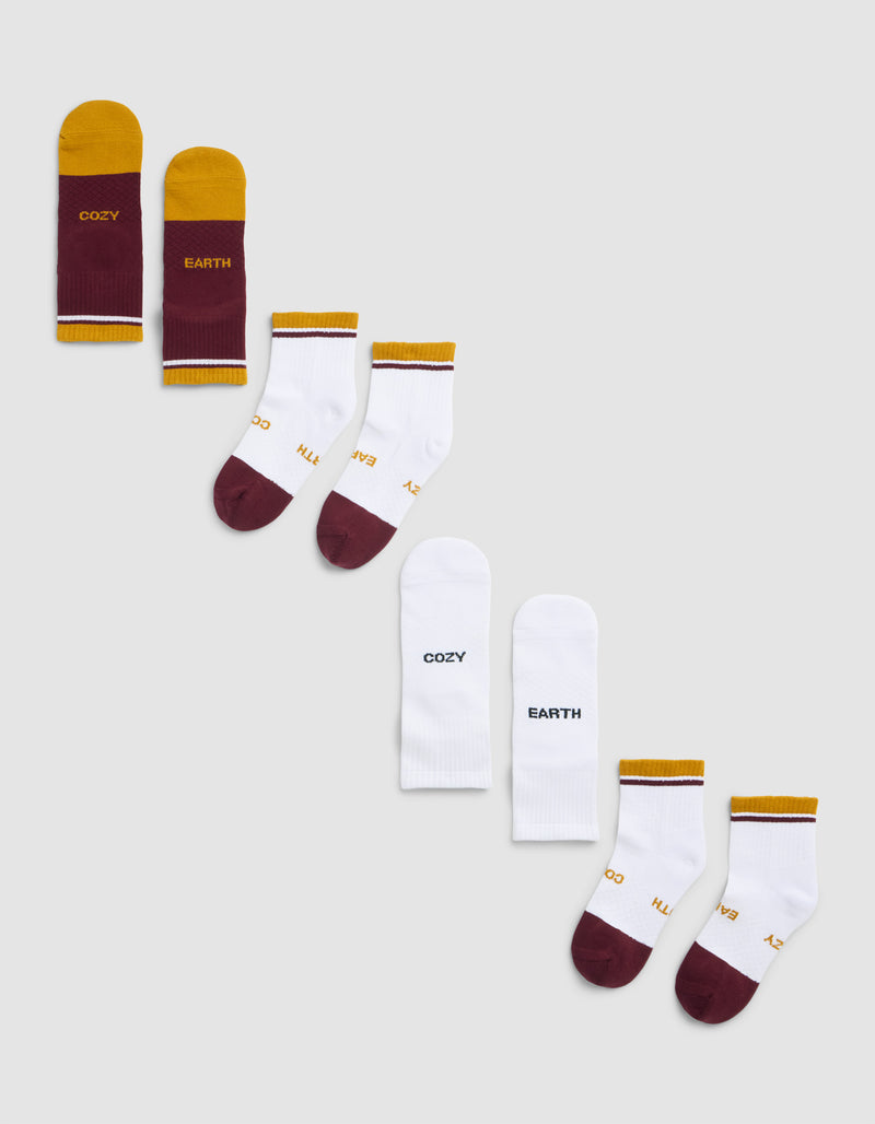 Three pairs from the Cozy Earth Essential Quarter Sock 4-Pack are arranged diagonally on a light gray background, featuring maroon and yellow "COZY EARTH" socks, white socks with gold accents, and plain white "COZY EARTH" socks.