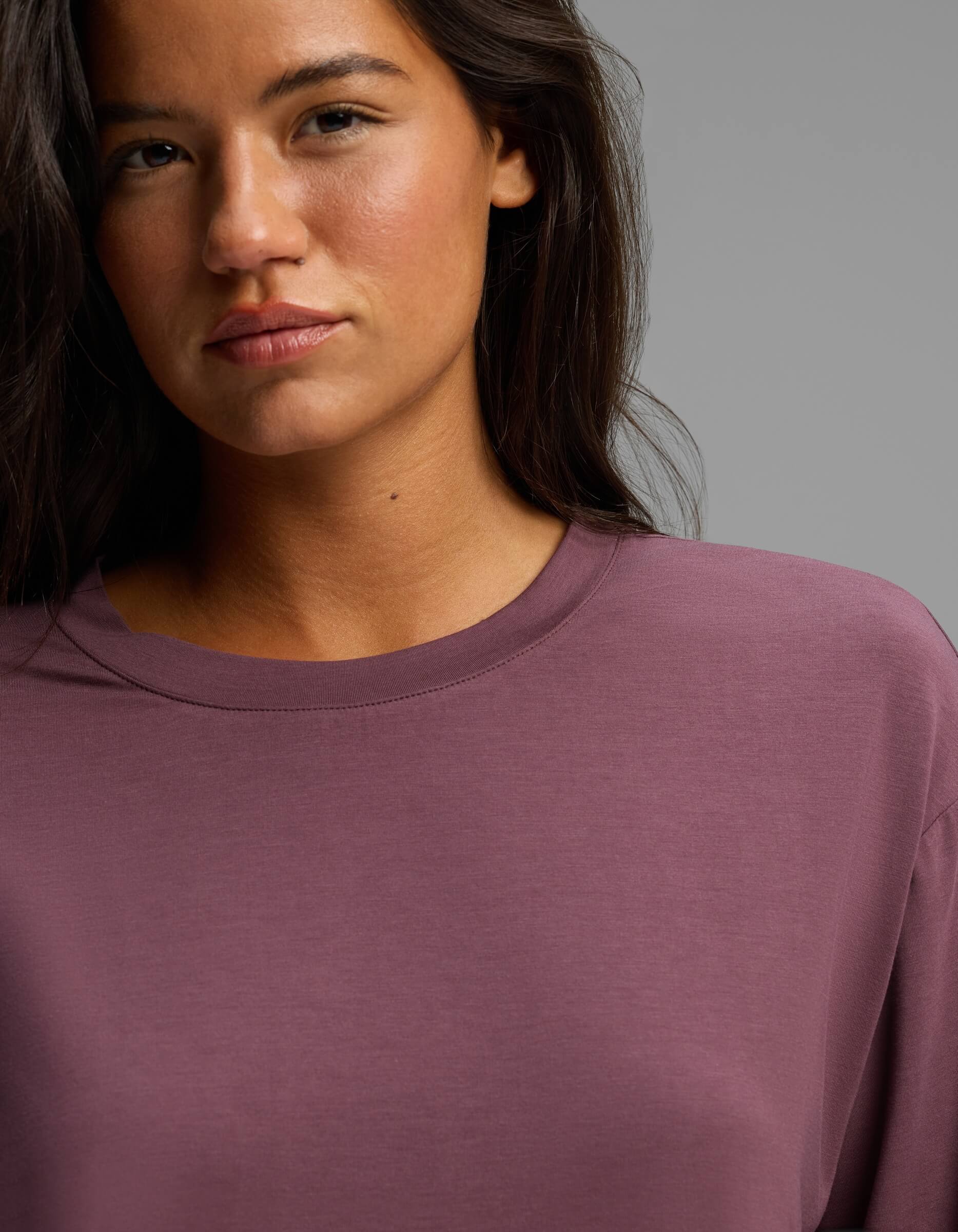 A woman with long dark hair, wearing the Cozy Earth Women’s First Layer Long Sleeve Sleep Tee in mauve, stands against a plain background, looking directly at the camera with a neutral expression.