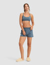 A woman poses against a light gray background, wearing the Women's First Layer Pajama Soft Bra & Boxer Short Set by Cozy Earth. She has long hair tied back, resting one hand on her waist and letting the other hang naturally.|Color:Dawn