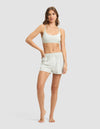 A woman stands barefoot against a plain background, wearing Cozy Earth's Women's First Layer Pajama Soft Bra & Boxer Short Set. She has one hand on her hip and looks forward with a relaxed expression.|Color:Laurel