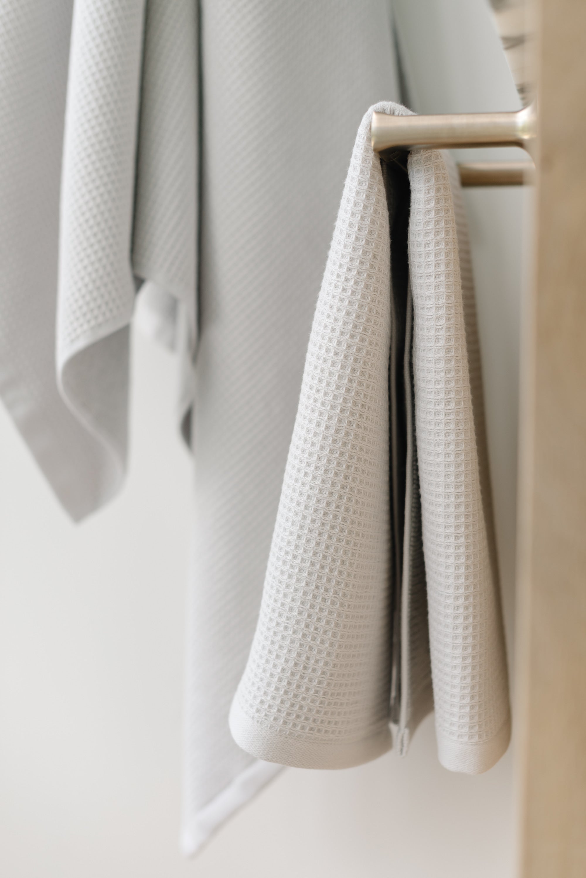 Waffle Hand Towel in the color Light Grey. Photo of Light Grey Waffle Hand Towel taken with the Light Grey Waffle Hand Towel hung from a towel ring. The picture was taken in a bathroom. 