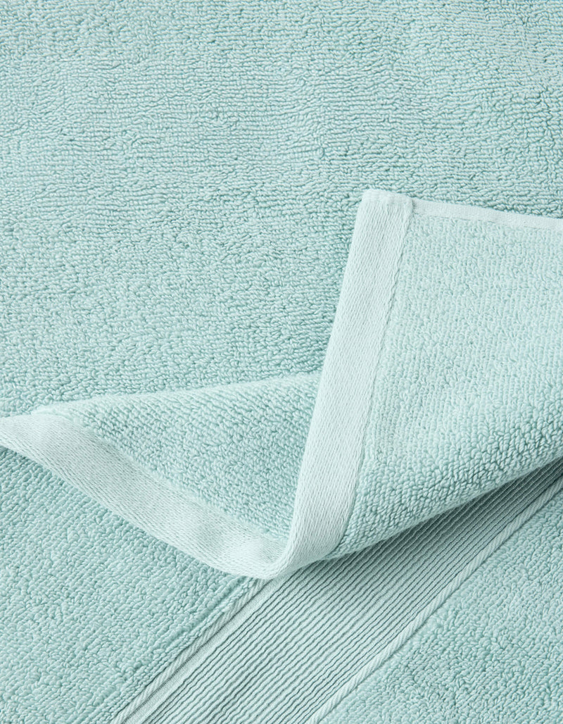 A close-up of a Luxe Bath Towel by Cozy Earth in light blue highlights its textured, soft, and absorbent fabric with detailed stitching and a neatly folded corner.