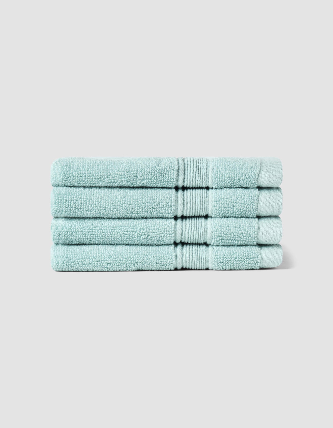 Four Luxe Washcloths by Cozy Earth, neatly folded in light blue, are stacked uniformly against a plain light gray background.|Color:Tide