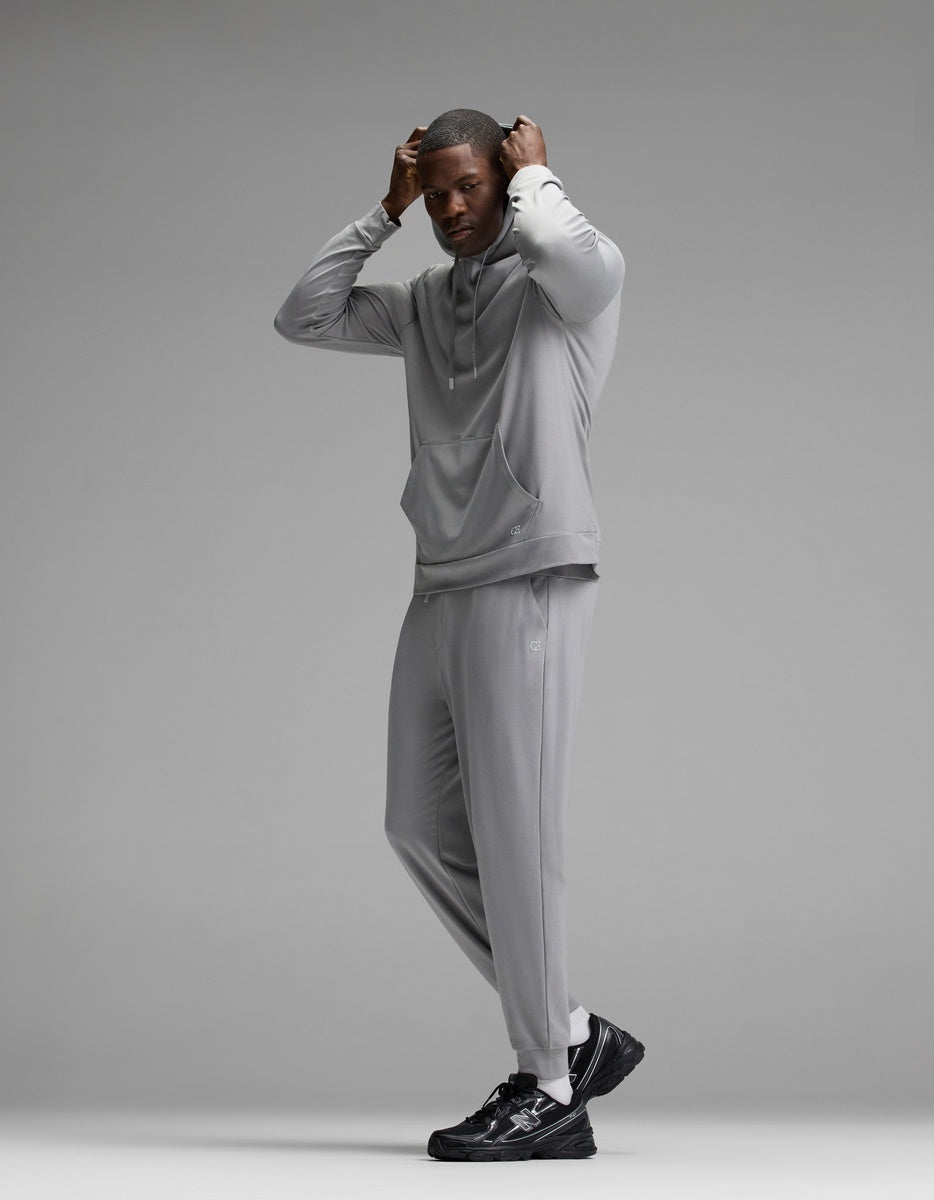 A man stands posing in the Cozy Earth Men’s Brushed Bamboo Hoodie & Jogger Set paired with black sneakers against a plain gray background.