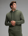A man stands wearing the Cozy Earth Men’s Brushed Bamboo Hoodie in olive green, paired with matching pants. He looks to his left with his hands clasped, set against a plain light gray background.|Color:Olive