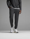 A person stands against a plain gray background wearing Cozy Earth’s Men’s Brushed Bamboo Joggers in Charcoal, paired with a matching long-sleeve top layered over a white undershirt and finished with white athletic sneakers. The upper body is partially out of frame.|Color:Charcoal