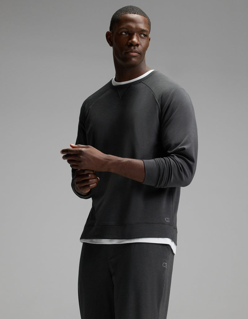 A man wears the Cozy Earth Men’s Brushed Bamboo Jogger Set in dark gray and stands against a plain gray background, looking to his left with a neutral expression and his hands loosely clasped.