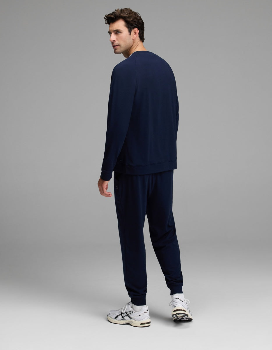 A man dressed in the Cozy Earth Men’s Brushed Bamboo Jogger Set and white sneakers stands facing slightly away, looking back over his shoulder against a plain gray background.