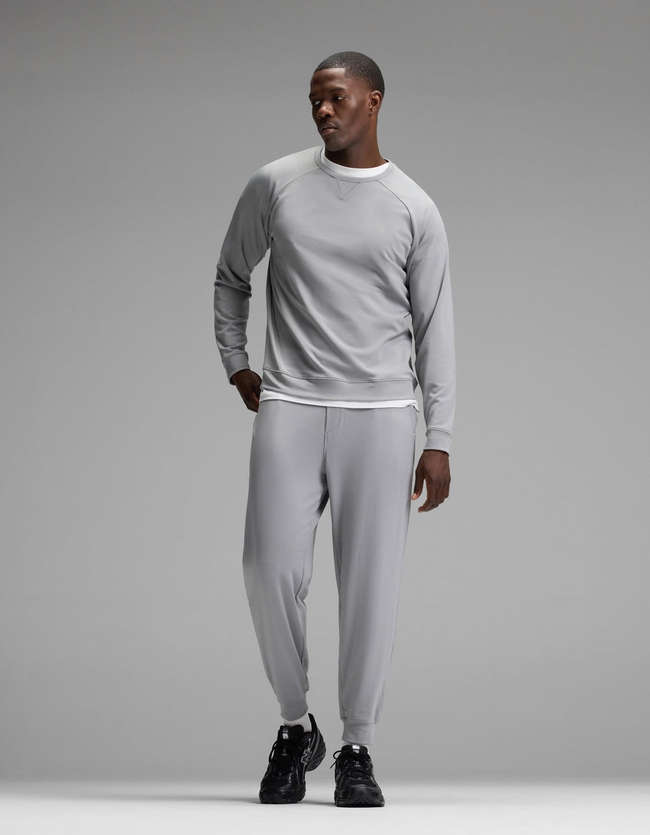 A man stands against a plain gray background wearing the Cozy Earth Men’s Brushed Bamboo Jogger Set in light gray, paired with black sneakers, looking to his left with one hand in his pocket.|Color:Stone