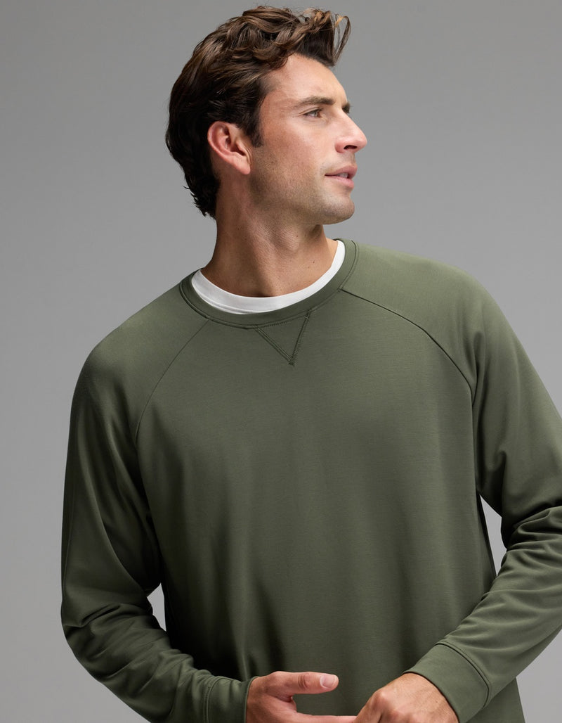 A man with short brown hair, wearing the Cozy Earth Men’s Brushed Bamboo Pullover Crew in olive green over a white shirt, stands against a plain gray background and looks to his left.