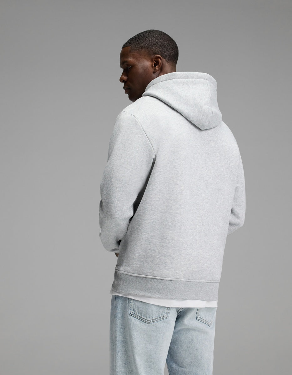 A person wearing the Cozy Earth Men’s Cityscape Hoodie in light gray and light blue jeans stands facing away from the camera against a plain gray background.