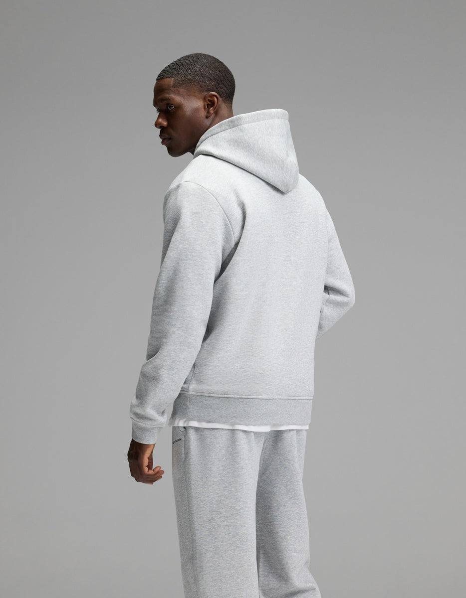 A man models the Cozy Earth Men’s Cityscape Hoodie & Sweatpant Set in light gray, standing against a plain gray background and glancing over his left shoulder.