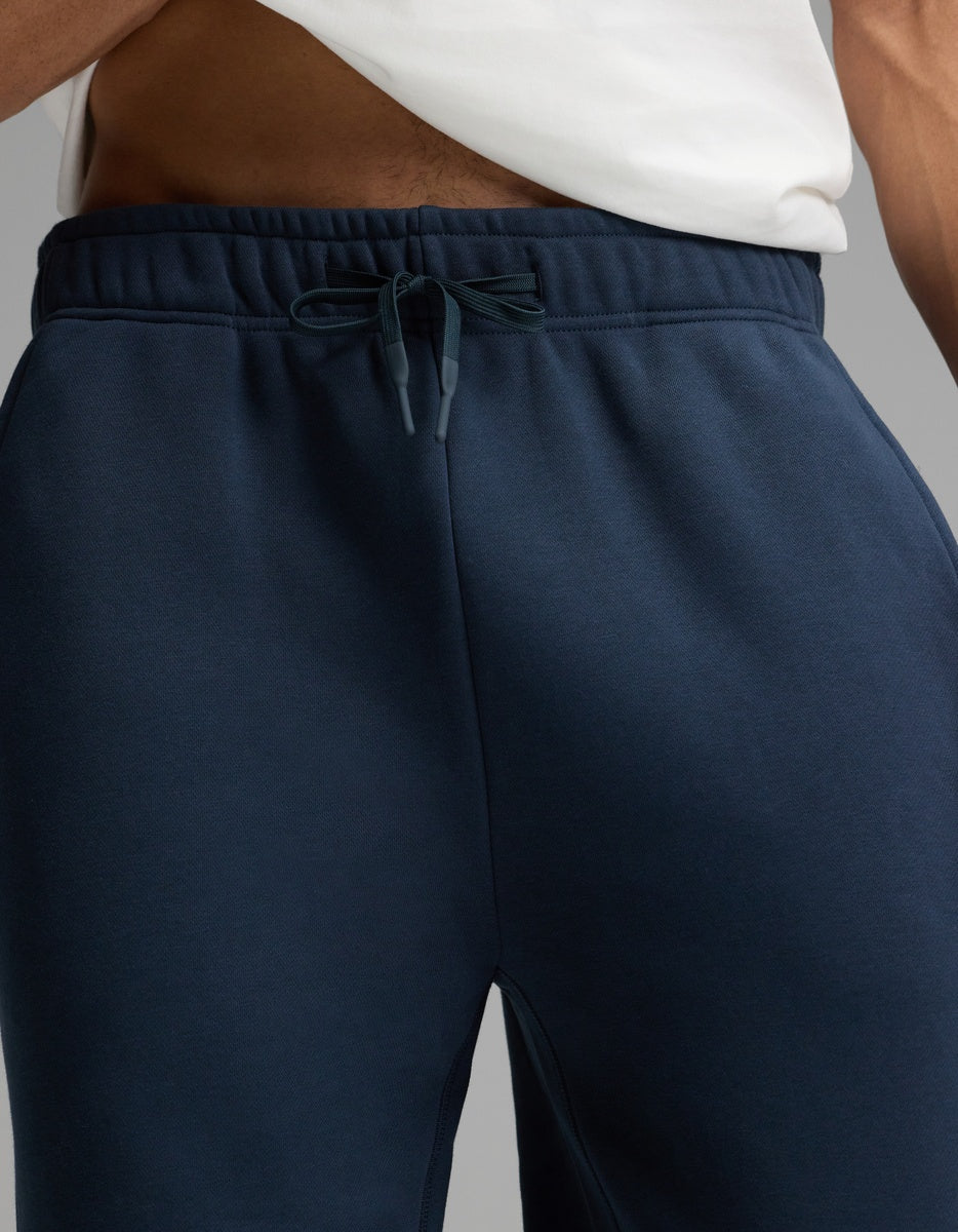 A person wearing a white shirt and Cozy Earth’s Men’s Cityscape Sweatpant in navy blue; the image is cropped to show only the lower torso and upper legs.