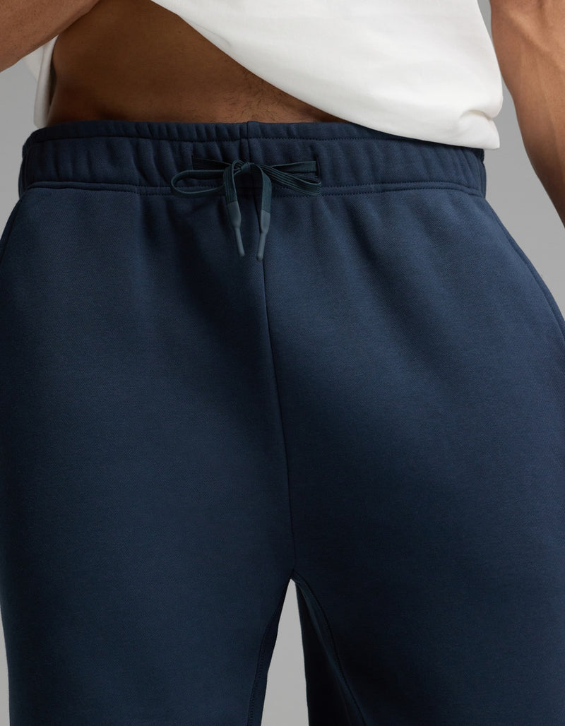 A person wearing a white shirt and Cozy Earth’s Men’s Cityscape Sweatpant in navy blue; the image is cropped to show only the lower torso and upper legs.