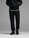 A person standing with hands in the pockets of Cozy Earth Men’s Cityscape Sweatpant in Jet Black, paired with a black sweatshirt, white shirt underneath, and black sneakers. The upper face is not visible.|Color:Jet Black