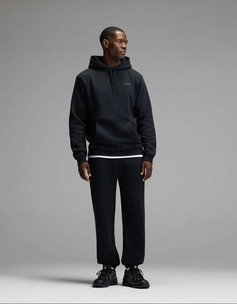 A man wearing Cozy Earth’s Men’s Cityscape Sweatpant in black, along with a matching black hoodie and sneakers, stands against a plain gray background, looking to his left.
